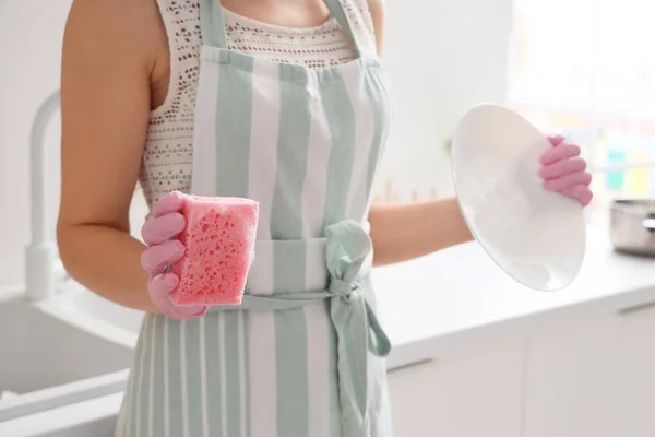 Woman with plate and cleaning sponge in kitchen, closeup