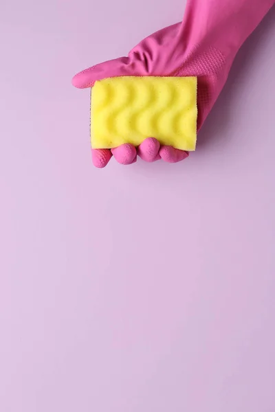 Hand in rubber glove holding yellow sponge on lilac background