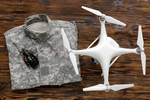 Modern quadcopter, military uniform and grenade on wooden background