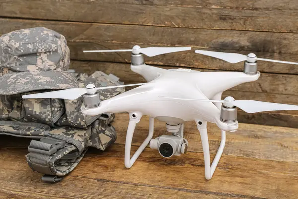Modern quadcopter, military cap and body armor on wooden background