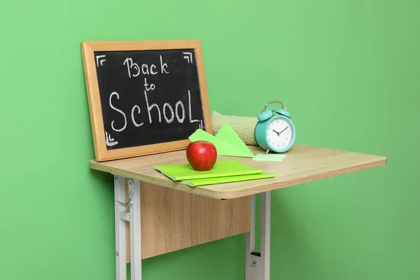 Modern school desk, stationery and blackboard with text BACK TO SCHOOL in room near green wall