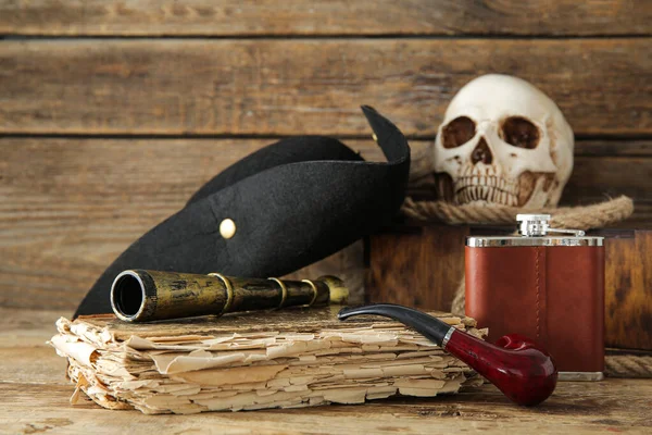 Chest with human skull, pirate hat, old manuscripts and travel equipment on brown wooden background