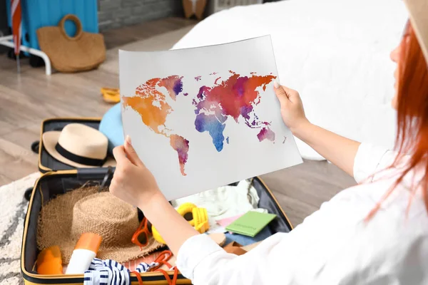 Young woman with world map unpacking suitcase in bedroom, closeup
