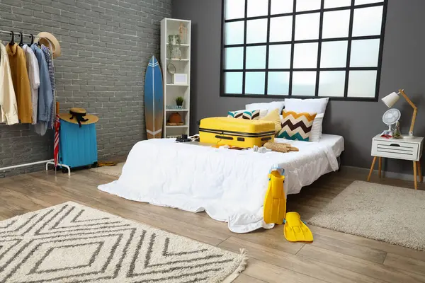 Interior of bedroom with suitcase and summer accessories on bed