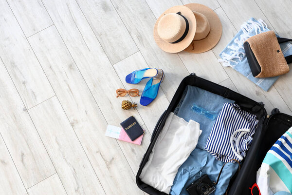 Open suitcase with beach accessories on light wooden floor, top view