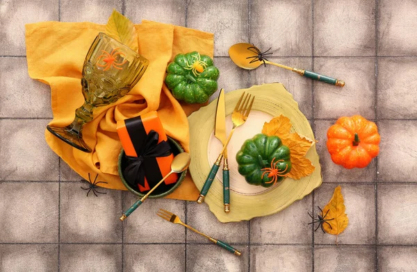 Halloween table setting with gift box and dry leaves on color tile background