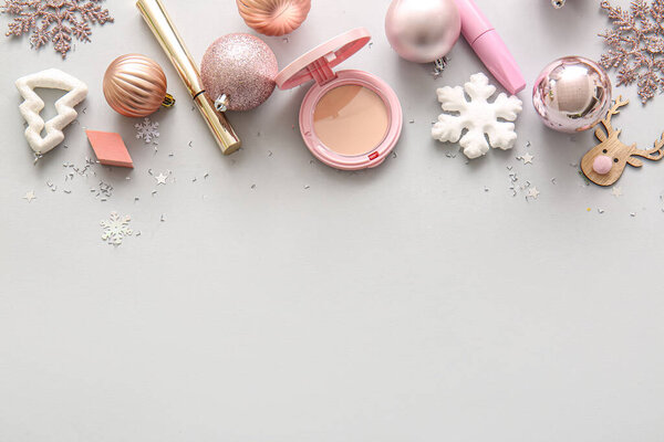Розовые рождественские украшения и макияж на сером фоне