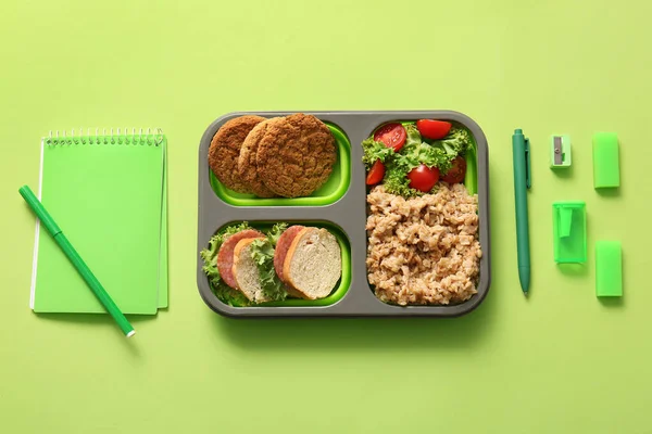 有美味食物和绿色背景的不同文具的午餐盒 — 图库照片
