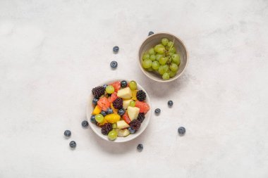 Hafif arka planda bir kase taze meyve salatası ve üzüm.