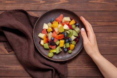 Ahşap arka planda taze meyve salatası tabağı olan bir kadın.