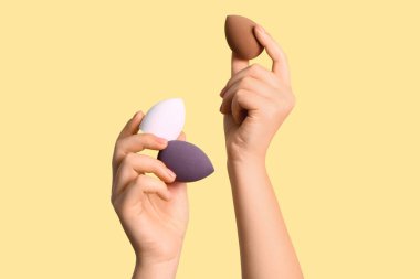 Bej arka planda farklı makyaj süngerleri olan kadın elleri