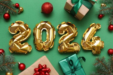 Şekil 2024 hediye kutuları ve yeşil arka planda Noel süsleri olan balonlardan yapılmış.