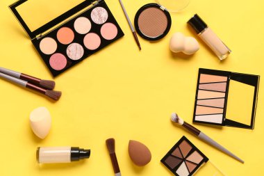 Sarı arka planda makyaj aksesuarları ve kozmetik ürünlerinden yapılmış çerçeve