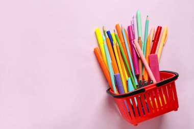 Pembe arka planda farklı kırtasiye malzemesi olan alışveriş sepeti