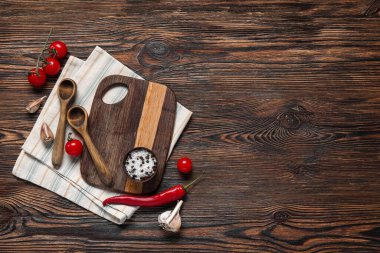 Kahverengi ahşap mutfak masasında kaşık ve taze ürünlerle kesim tahtası.