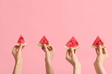 Pembe arka planda olgun karpuz dilimleriyle kadın elleri