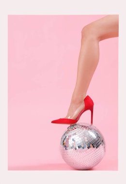Şık topuklu kadın bacağı, çerçeveli ve pembe arka planda disko topu.