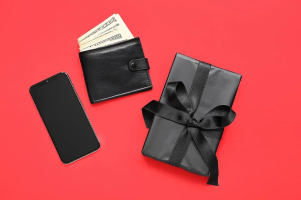 Gift box, mobile phone and wallet with money on red background. Black Friday concept