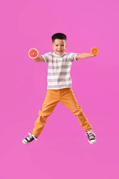 亚洲小男孩 带着新鲜柚子片和紫色背景的橙色跳跃 — 图库照片