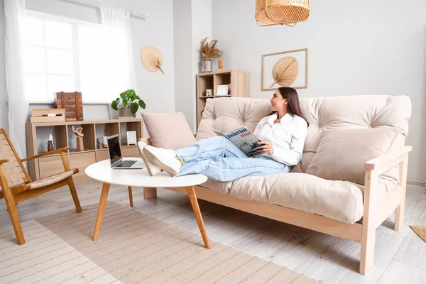 stock image Young woman reading magazine on couch in living room