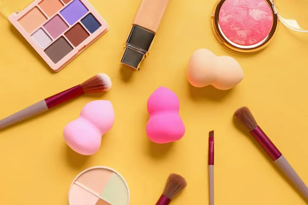 Composition with makeup sponges, brushes and cosmetics on yellow background