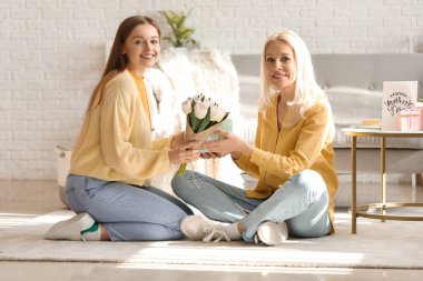 Genç bir kadın, annesini lalelerle ve hediyelerle selamlıyor.