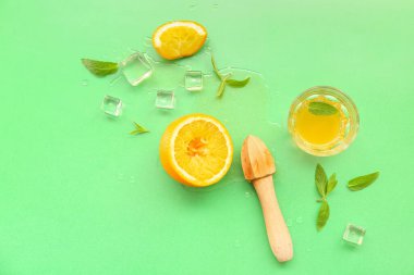 Meyve sıkacağı, cam, buz küpleri ve yeşil arkaplanda naneli portakal suyu.