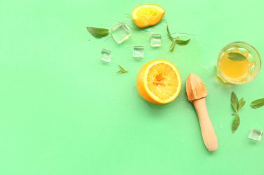 Meyve sıkacağı, cam, buz küpleri ve yeşil arkaplanda naneli portakal suyu.