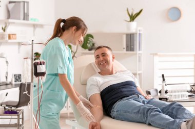 Kadın hemşire klinikte kan donörünün koluna yama uyguluyor.