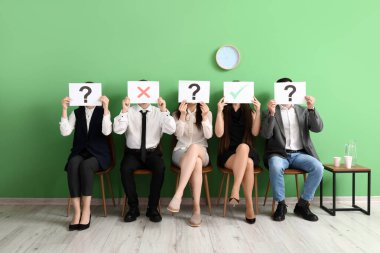 Genç adaylar odada farklı notlarla kağıt çarşaf tutuyorlar.