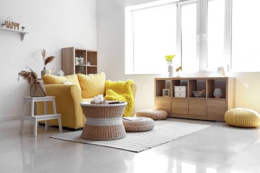 Işıl ışıl oturma odasının içinde şık sarı kanepe, sehpa ve hasır puflar.