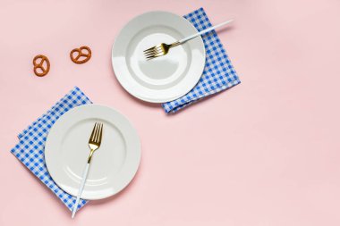 Boş tabaklar, çatallar, pembe arka planda mavi kareli peçeteler ve krakerler