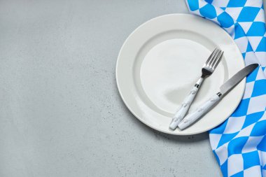 Boş tabak, çatal, bıçak ve gri masadaki mavi kareli masa örtüsü.