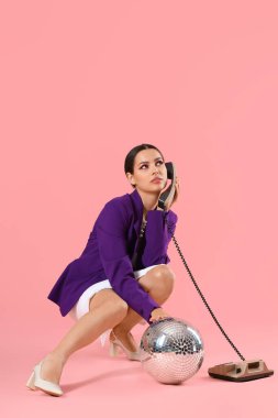 Disko toplu şık genç bir kadın pembe arka planda telefonla konuşuyor.
