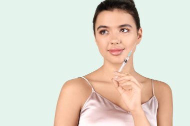 Yeşil arka planda güzel dudakları ve şırıngası olan genç bir kadın, yakın plan.