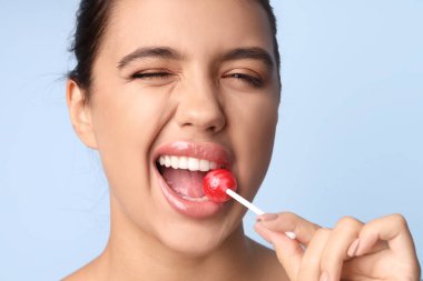 Güzel dudakları olan genç bir kadın mavi arka planda lolipop yiyor.