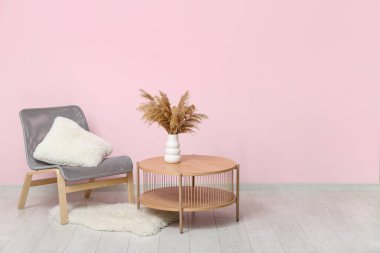 Rahat koltuk ve ahşap masa, pembe duvarın yanında otlar var.