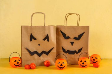 Bej arka planda Cadılar Bayramı için sepet ve balkabağı dolu alışveriş torbaları.