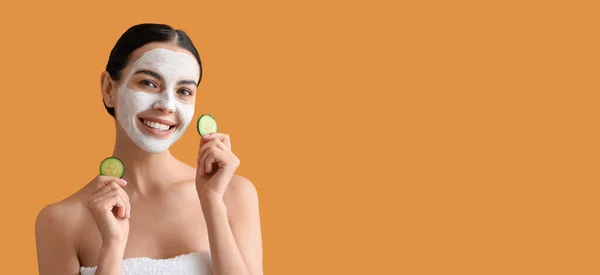 Beautiful young woman with cucumber slices and facial mask on orange background with space for text