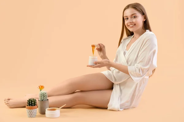 Young woman with sugaring paste and cacti on beige background