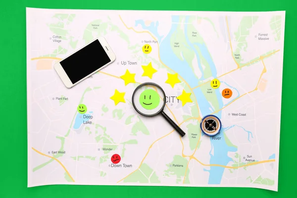 Map with rating smiles, stars, magnifier, compass and mobile phone on green background