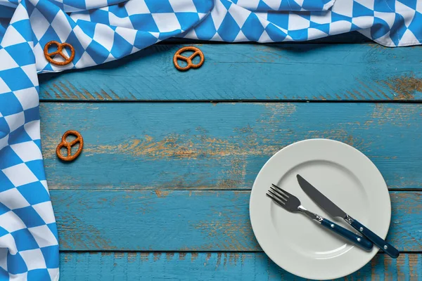 Beyaz tabak, çatal bıçak, kraker ve mavi ahşap arka planda kareli masa örtüsüyle Oktoberfest masası
