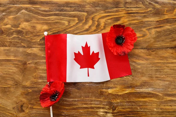 Poppy flowers with flag of Canada on brown wooden background. Remembrance Day