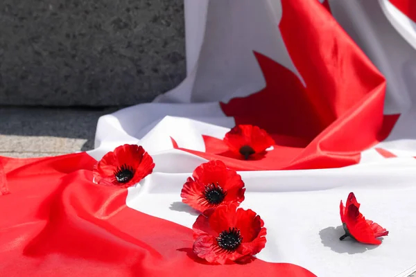 Many poppy flowers with flag of Canada on stone monument. Remembrance Day