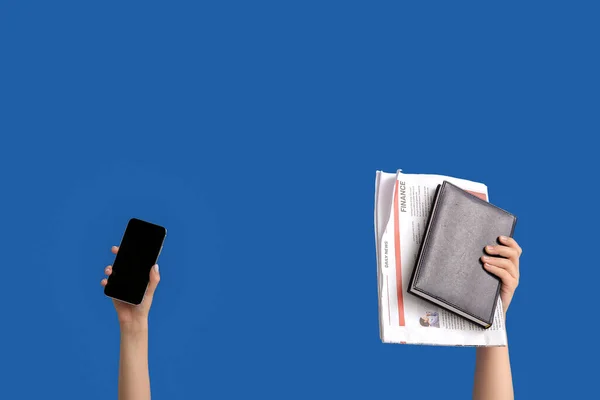 Female hands with mobile phone, notebook and newspaper on blue background