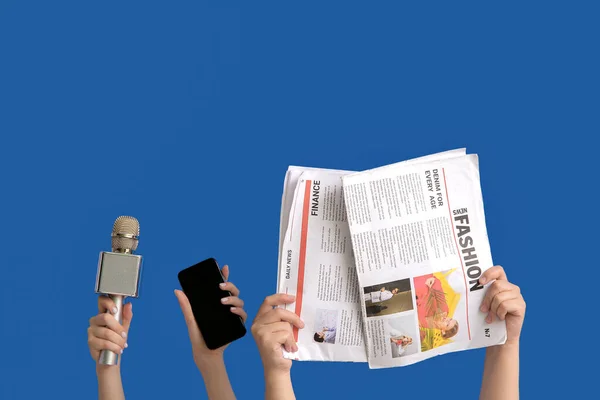 蓝色背景的手持话筒 手机和报纸的女性手 — 图库照片