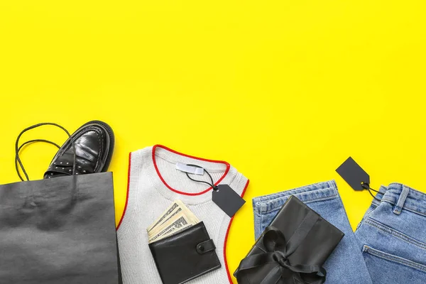 Stylish clothes, gift box and wallet with money on yellow background. Black Friday concept