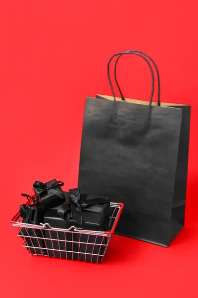 Shopping basket with gift boxes and bag on red background. Black Friday concept