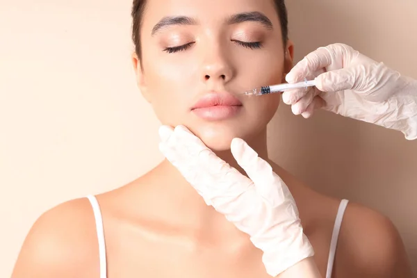 Young woman receiving lip injection on beige background, closeup