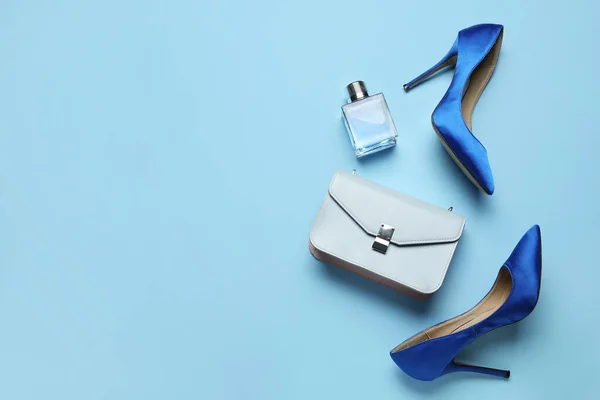 Stylish blue high heels with purse and perfume on color background